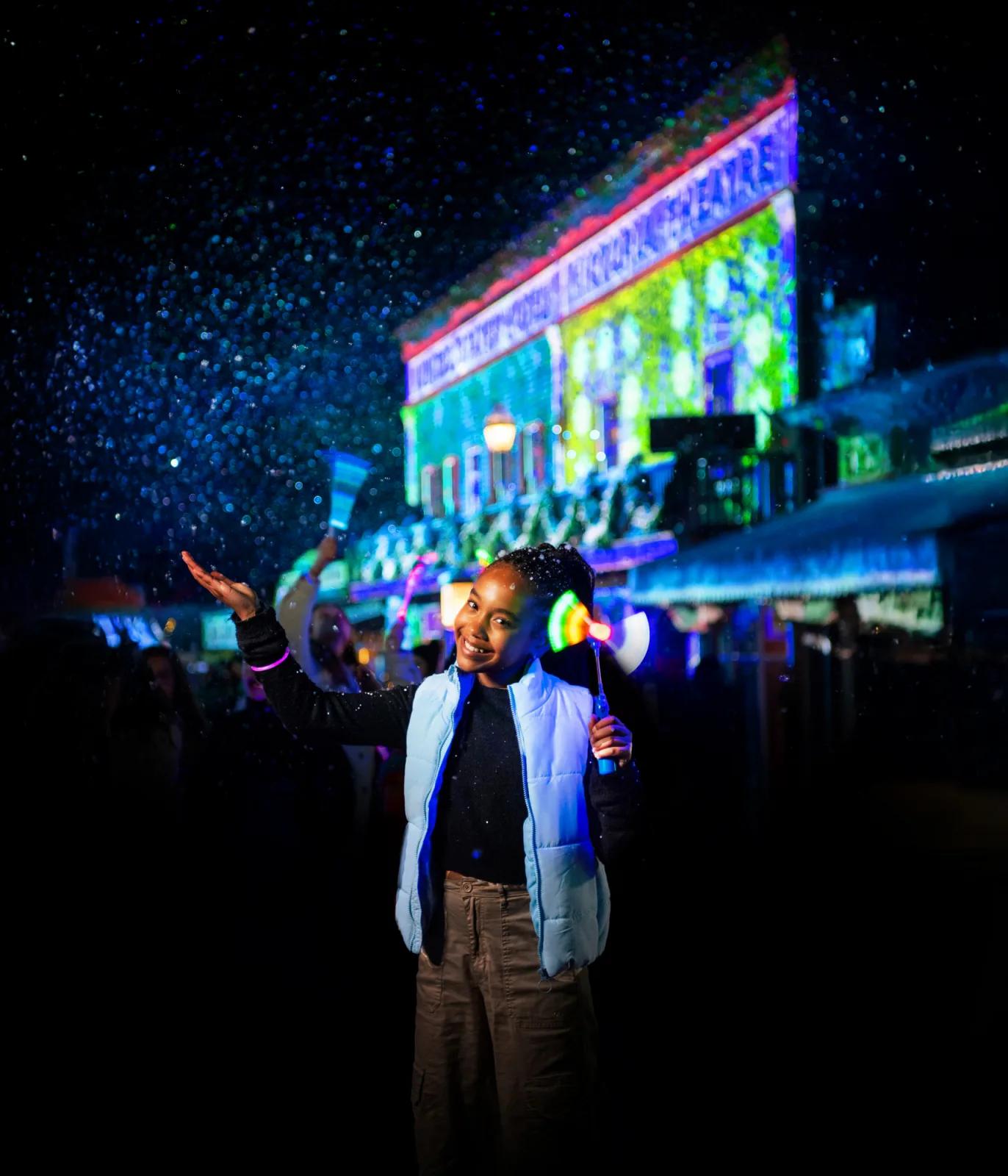 Child enjoying falling snow under colourful light projections on historic buildings, from Australia’s most visited outdoor museum and heritage attraction.