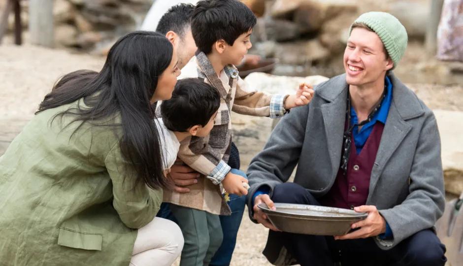 Visitor experience at Sovereign Hill's gold rush attraction, with a costumed interpreter showing gold panning techniques to a family.