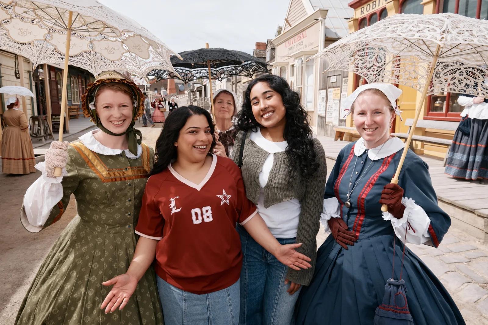 Two visitors posing with costumed women in 19th-century dress along Sovereign Hill’s historic Main Street.