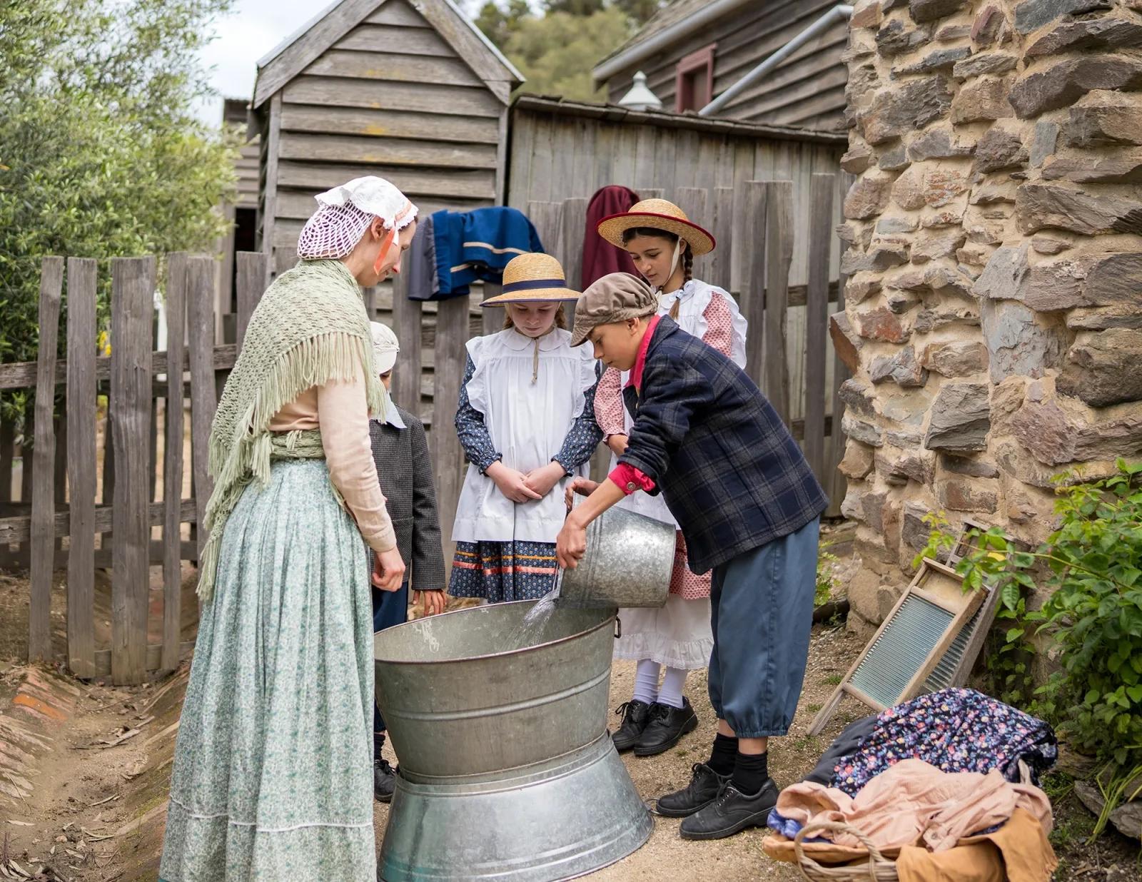 Costumed educators and school students gathered around a wash tub during a hands-on historical learning program at Sovereign Hill.