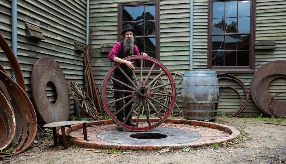 Justin Mc Cann Wheelwrights holding a restored wooden wagon wheel outside the historic workshop at Sovereign Hill.