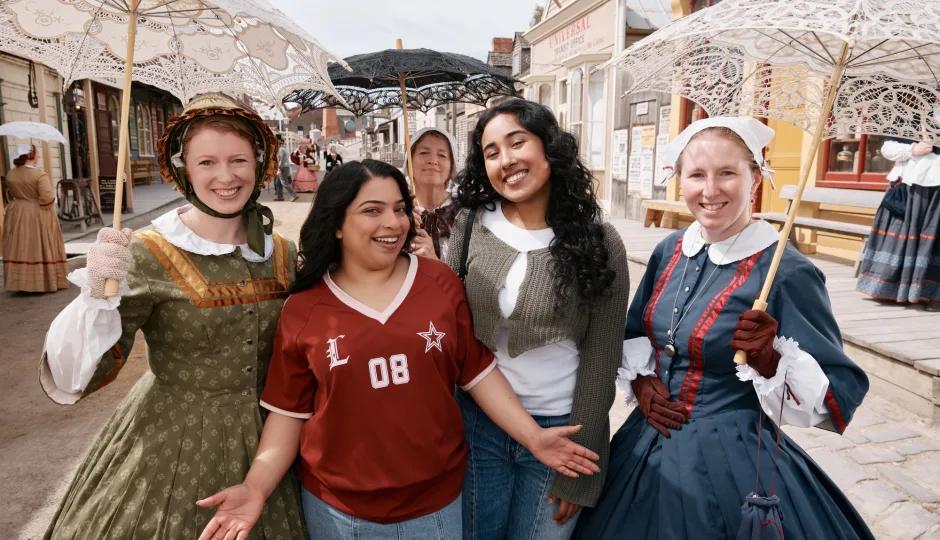 Two visitors posing with costumed women in 19th-century dress along Sovereign Hill’s historic Main Street.