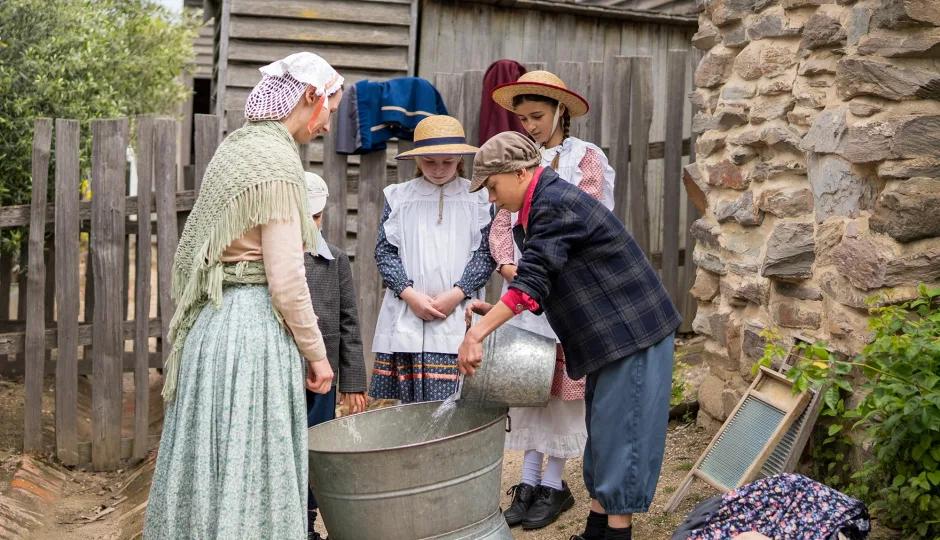 Costumed educators and school students gathered around a wash tub during a hands-on historical learning program at Sovereign Hill.