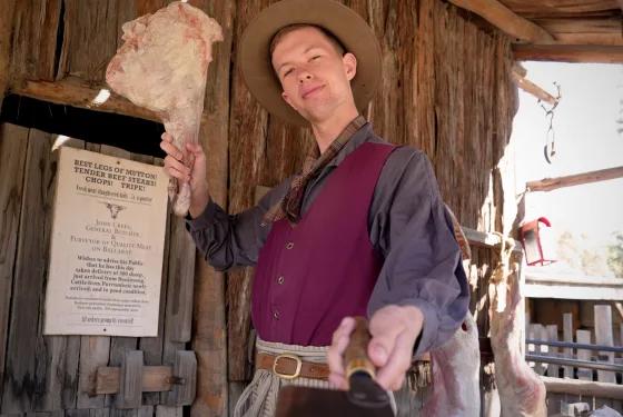 Goldfields butcher reenactor holding fresh meat outside a rustic wooden shop, from Australia’s most visited outdoor museum and heritage attraction.