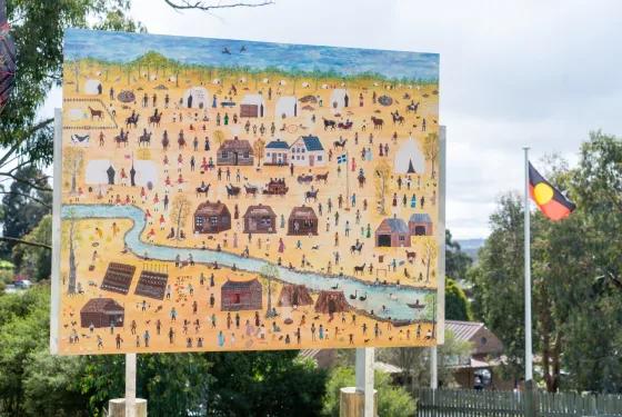 Illustrated Aboriginal goldfields scene displayed outdoors at Sovereign Hill, with an Aboriginal flag visible beside the artwork.