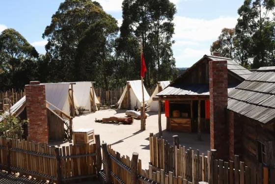 Reconstructed Chinese goldfields camp at Sovereign Hill with canvas tents, timber buildings and a red flag among surrounding trees.